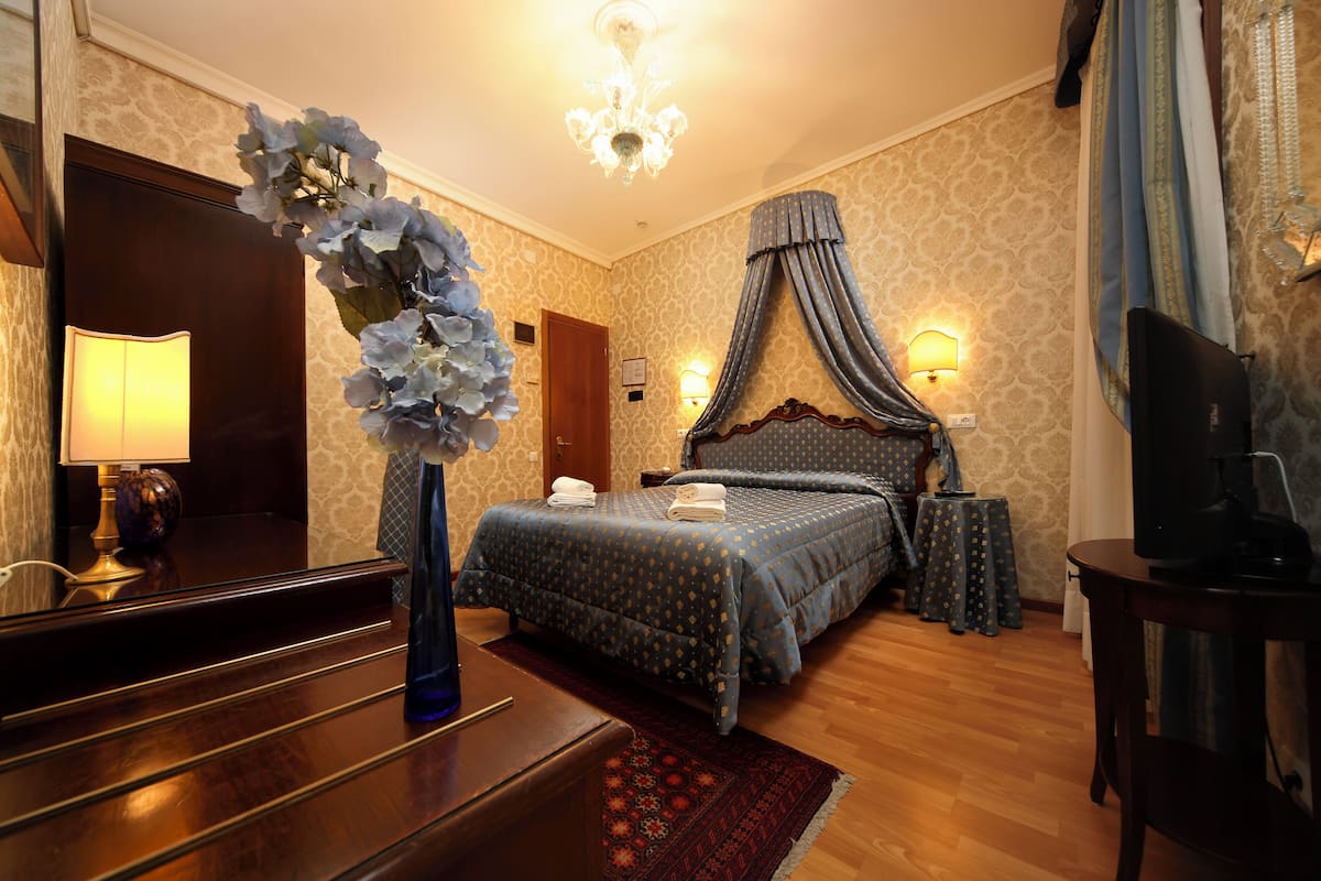 A hotel room with a large bed, a desk, a chair, a television, and a vase with flowers.