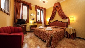Una habitación de hotel con una cama grande, televisión, un sillón rojo y un candelabro.