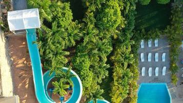 Une vue aérienne d’un parc aquatique doté de nombreux toboggans et de plusieurs piscines, entouré d’une végétation luxuriante et d’un mur de pierre.