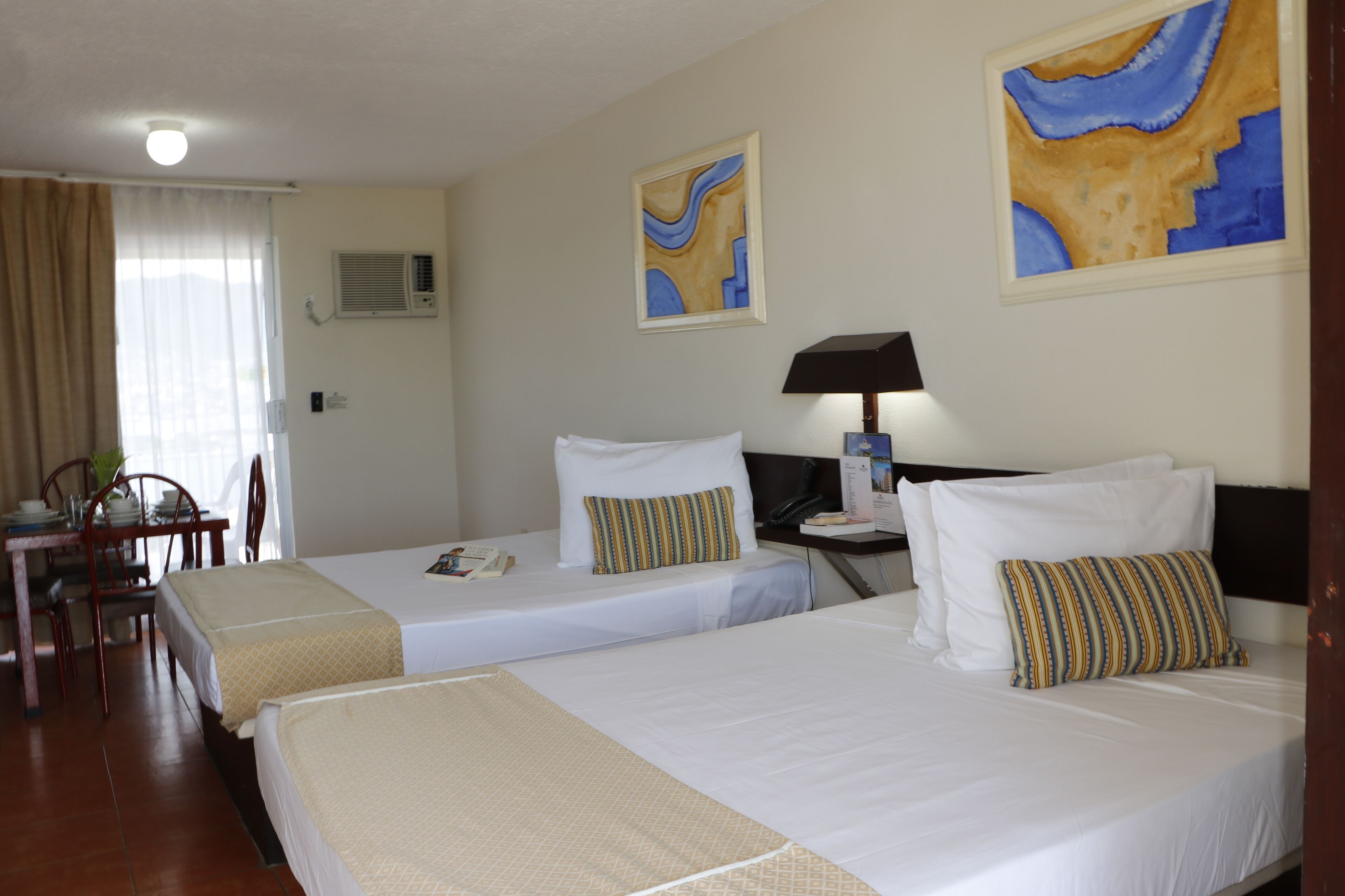 A hotel room with two beds, a desk, chairs, and artwork on the walls.