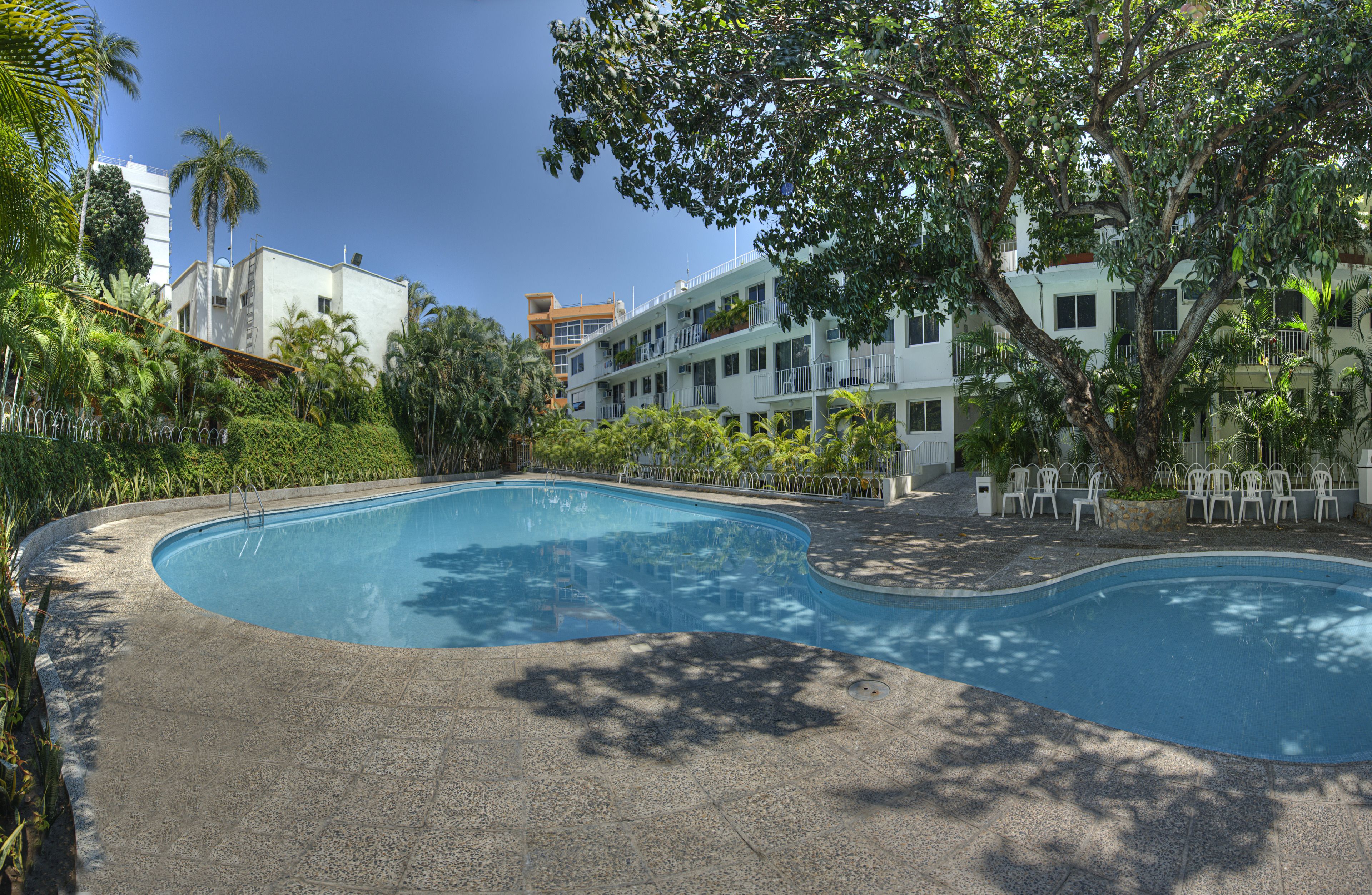 A swimming pool with a curved design, surrounded by a paved area and a fence.