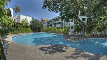 A swimming pool with a curved design, surrounded by a paved area and a fence.