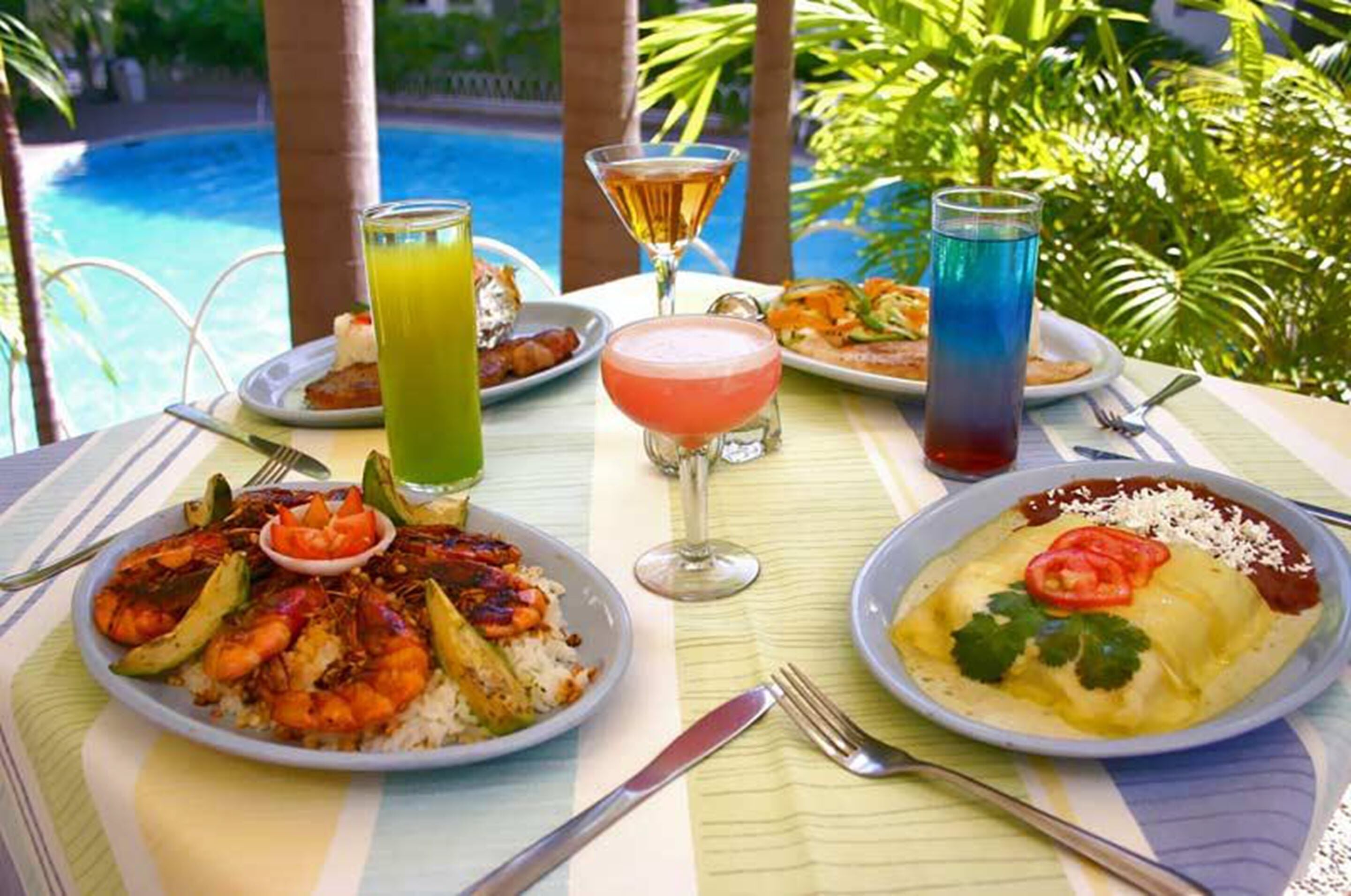 A dining table with plates of food, drinks, and a pool in the background.