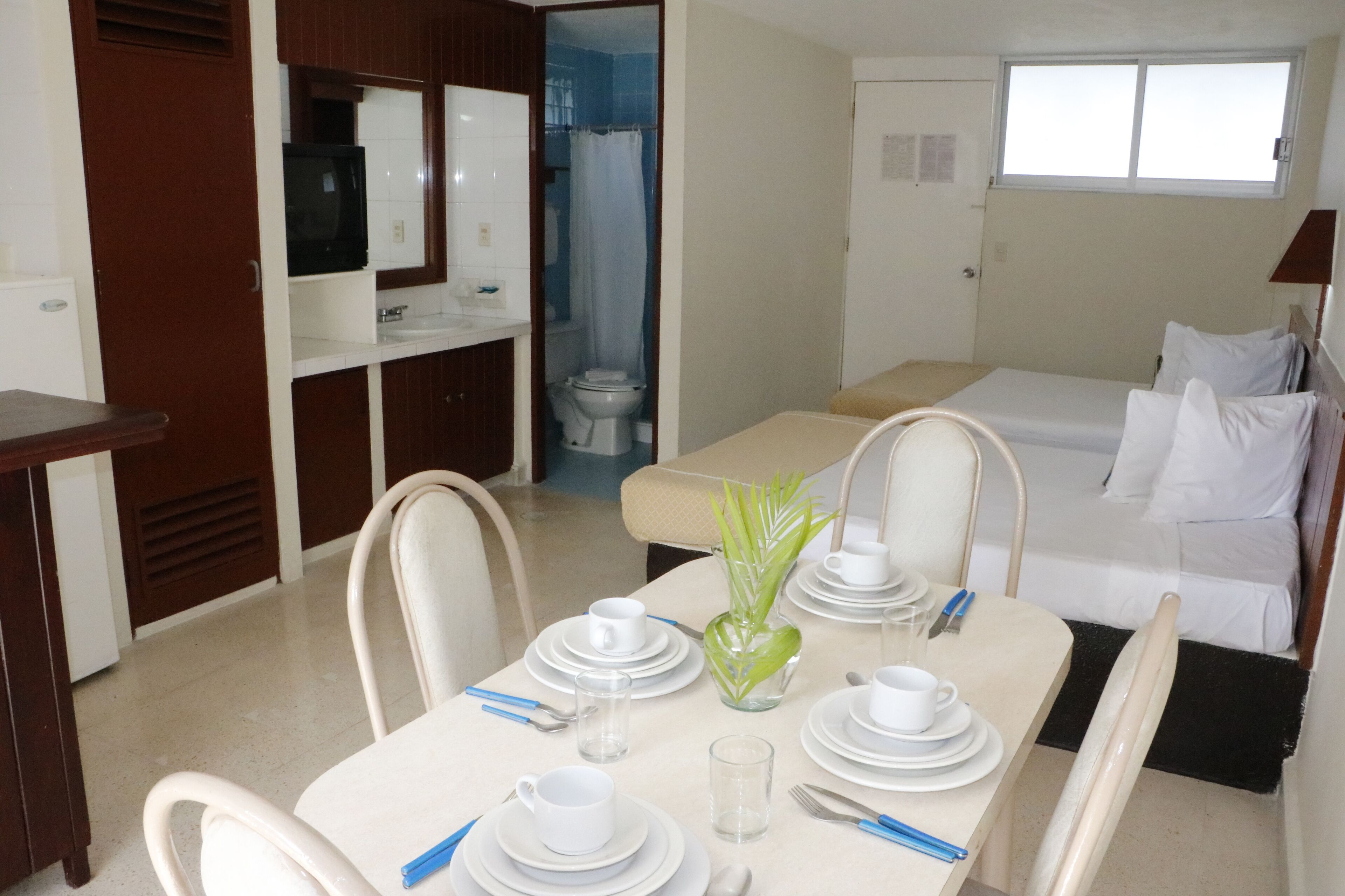 A hotel room with a dining area, a bed, a bathroom, and a TV.