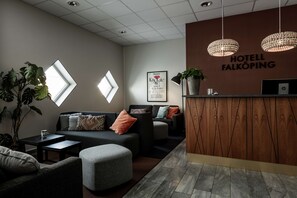 Een hotellobby met een receptiebalie, een zithoek en een groot raam dat natuurlijk licht binnenlaat.