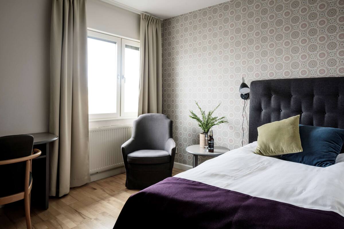 A bedroom with a bed, a chair, a small table with a plant, and a radiator.