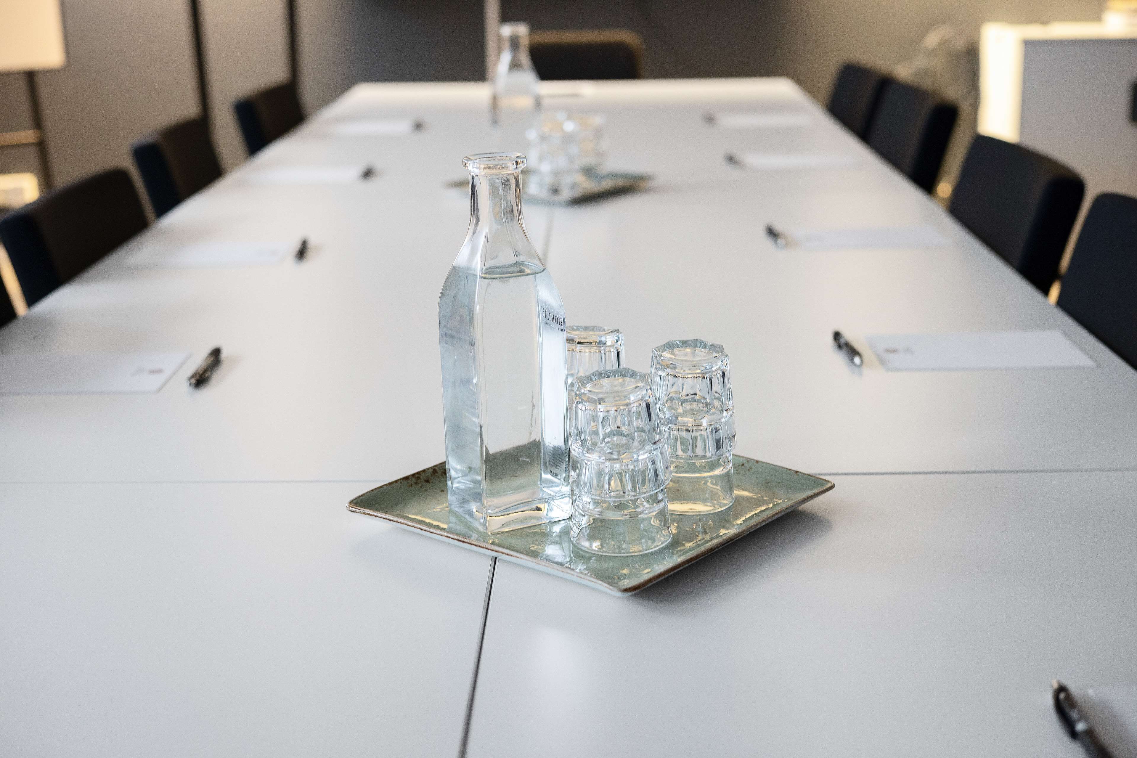 Ett konferensbord med en flaska, glas och pennor.