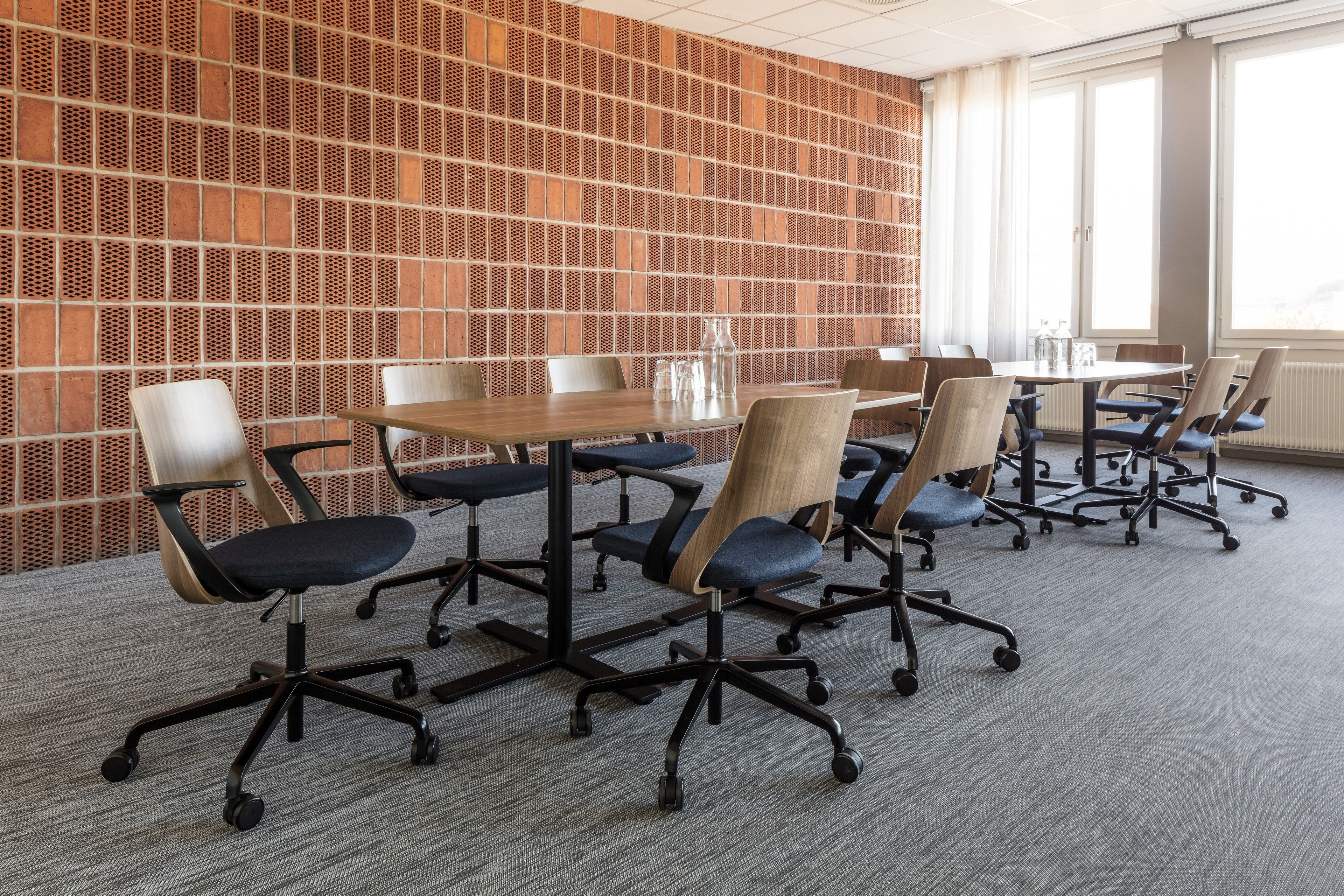 Uma sala de conferências com parede em padrão de tijolos, uma mesa grande e cadeiras de escritório modernas.
