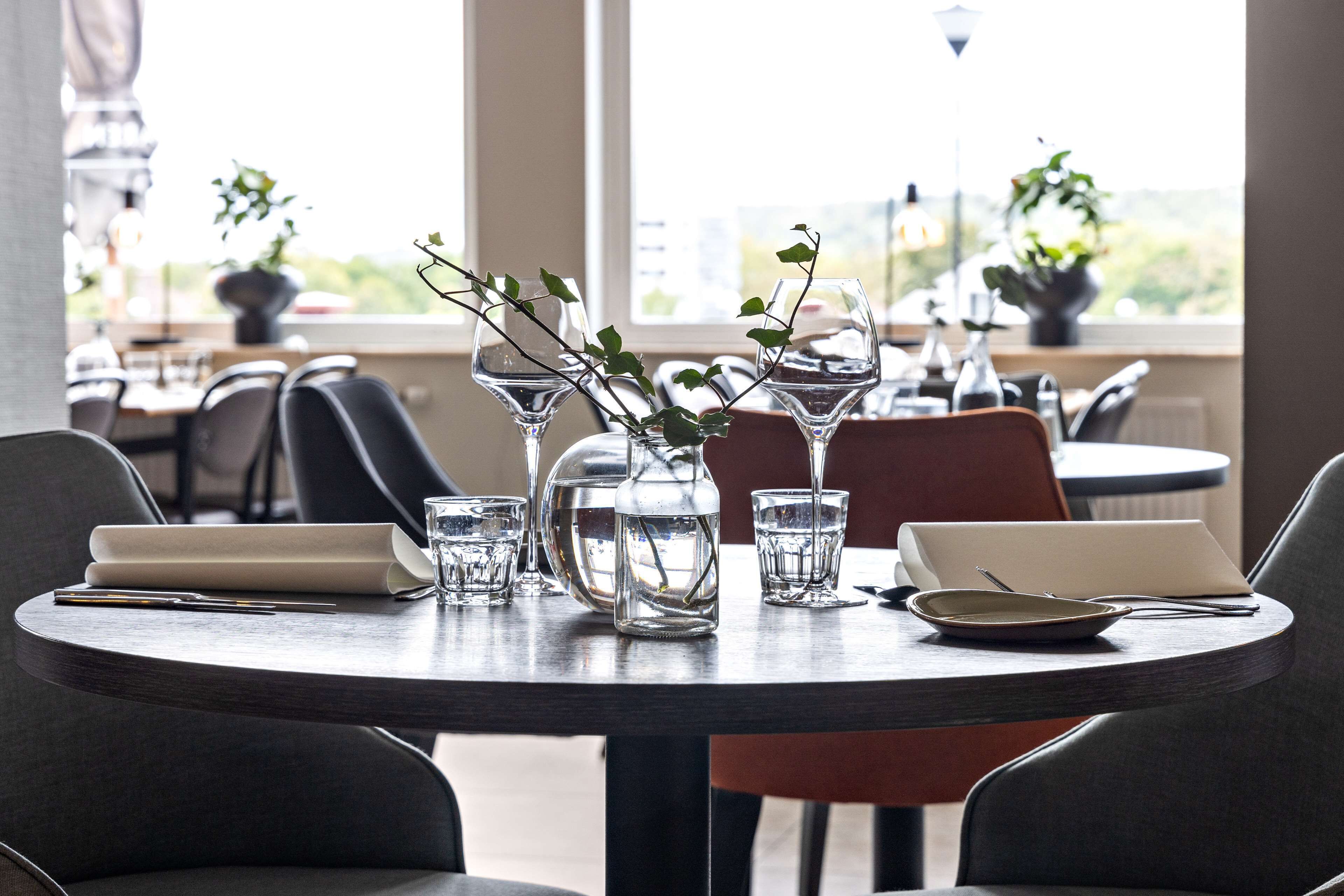 A dining table with a laptop, a vase with branches, and a bowl.