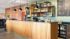 A bar area with a wooden counter, shelves with bottles, and a menu on the wall.