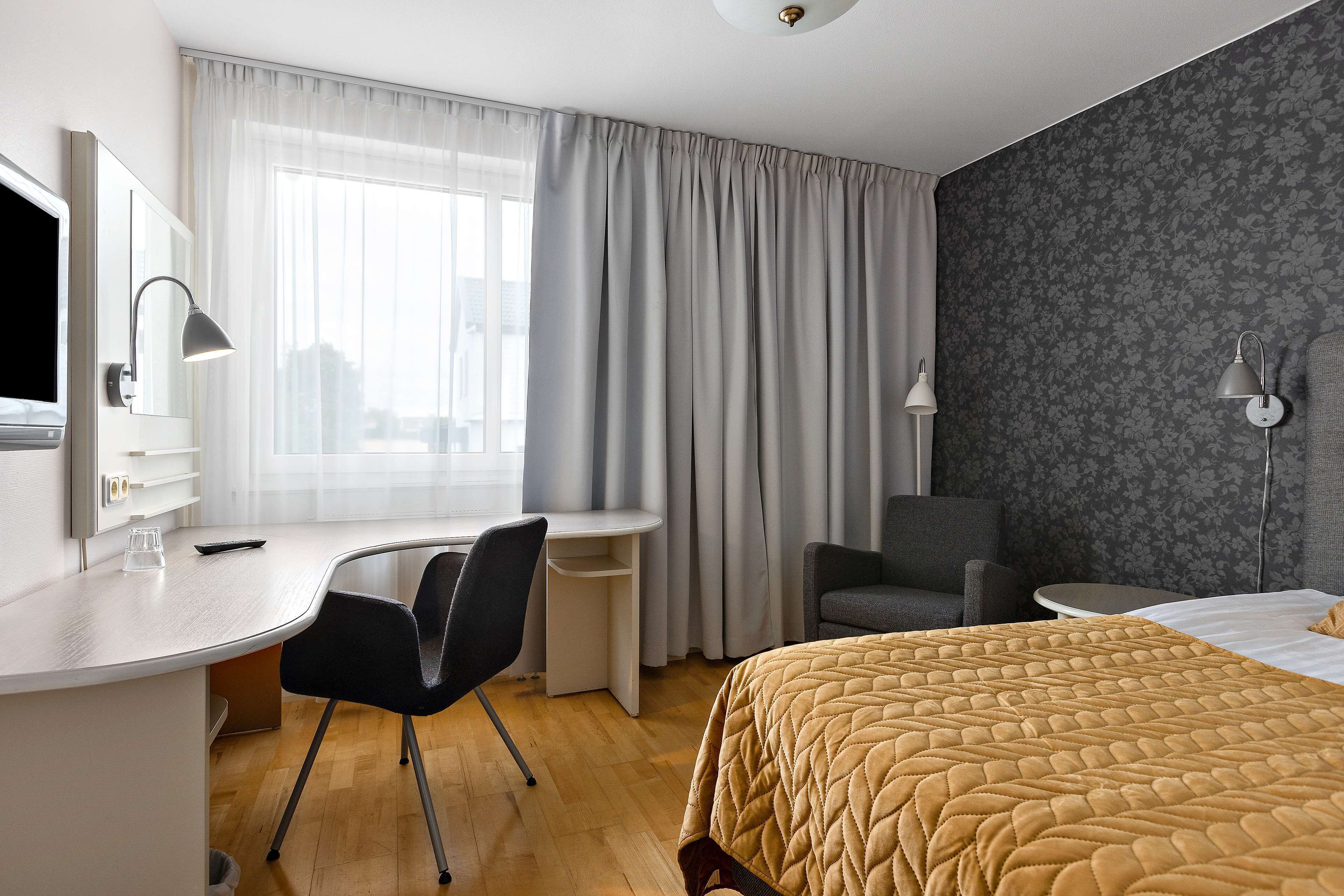 Et hotelværelse med en seng, et skrivebord med stol, et fjernsyn og en lampe.