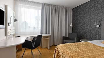 Et hotelværelse med en seng, et skrivebord med stol, et fjernsyn og en lampe.