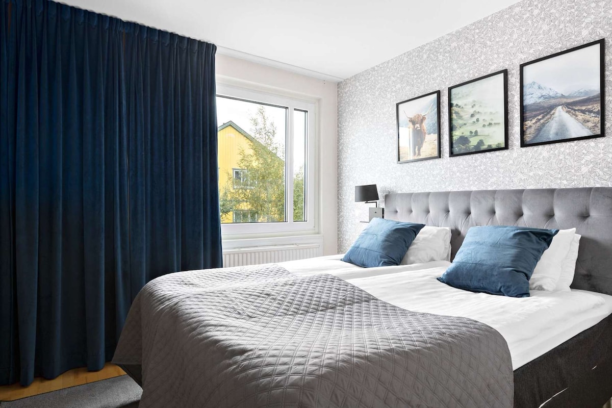 A bedroom with a large bed, a window with curtains, and three framed pictures on the wall.