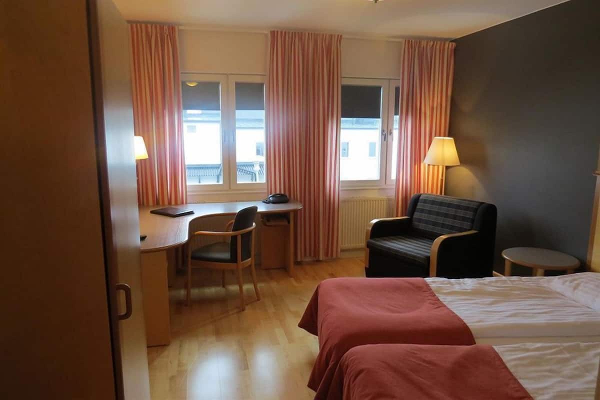A hotel room with two beds, a desk, a chair, a small table, and a window with curtains.