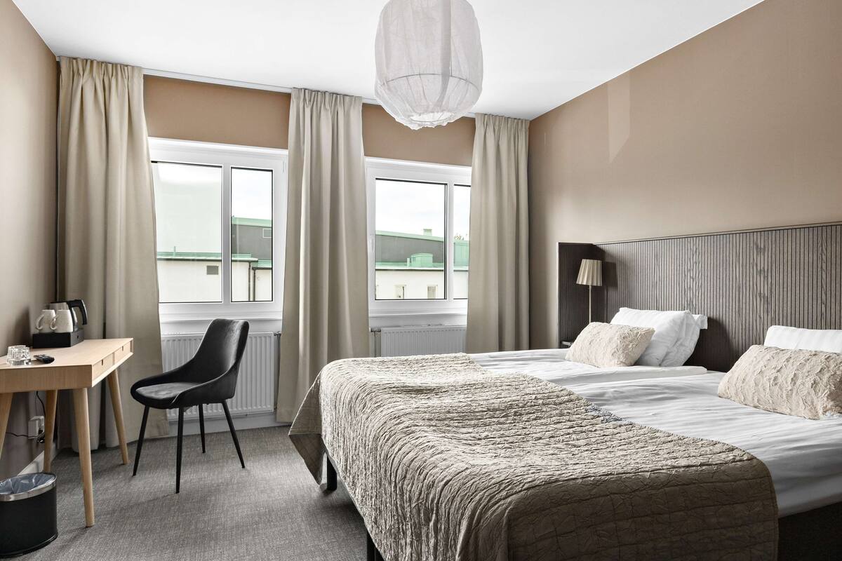 A hotel room with a bed, a desk, a chair, and a window with curtains.