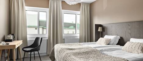 A hotel room with a bed, a desk, a chair, and a window with curtains.