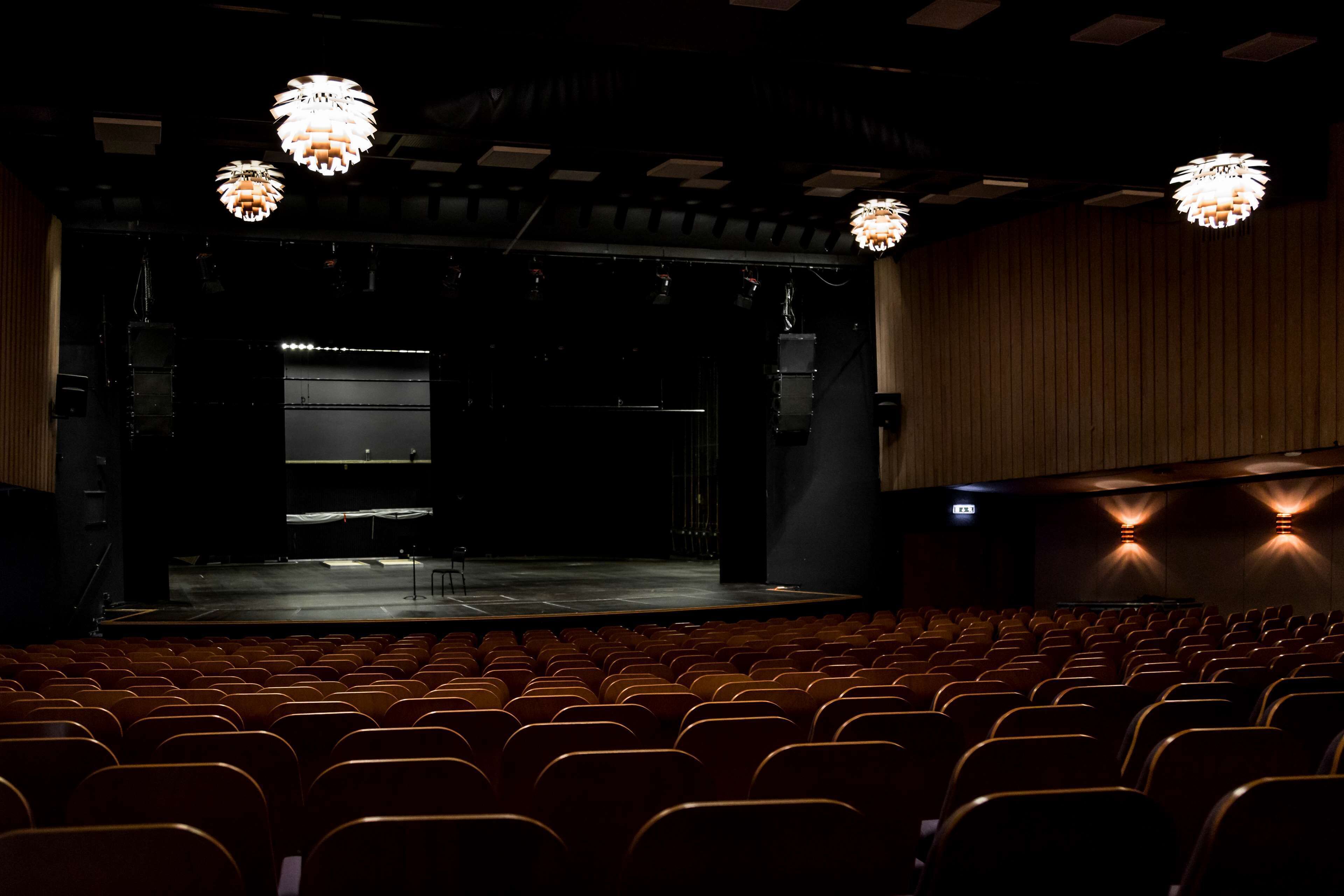 Un auditorio con hileras de asientos, un escenario y candelabros.