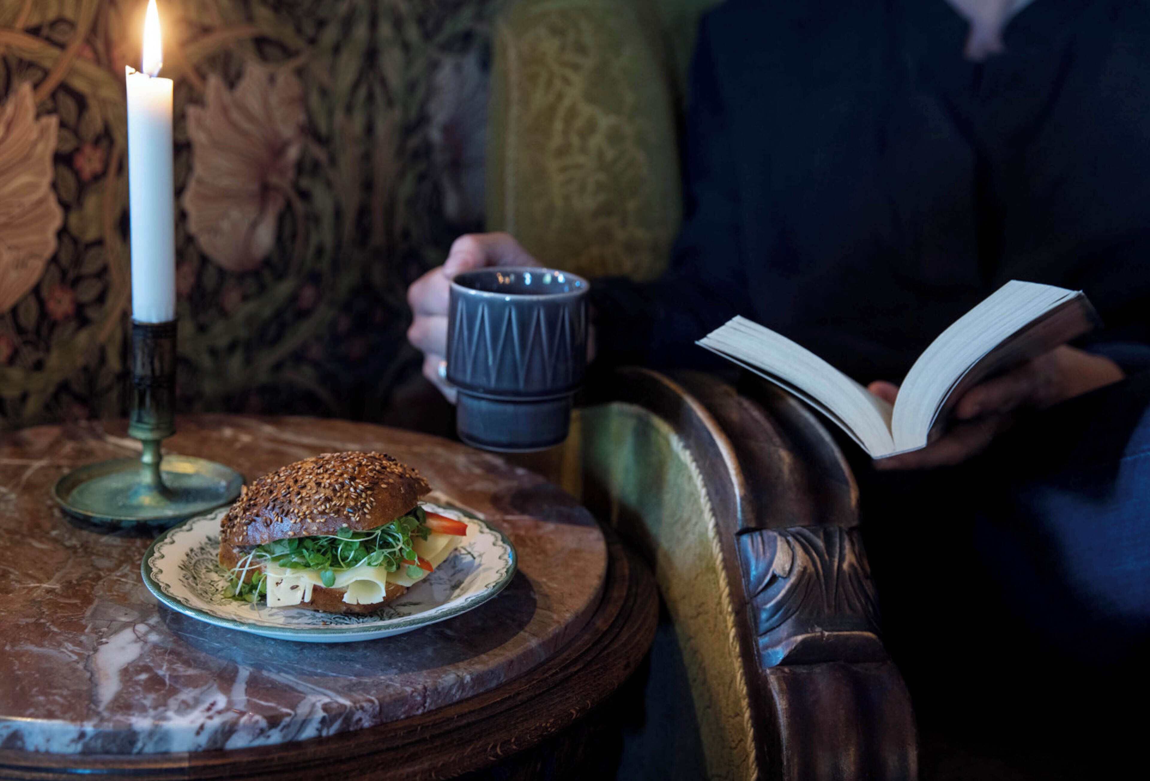 A candle, a book, and a sandwich on a table.
