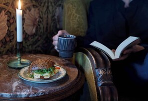 Una vela, un libro y un sándwich sobre una mesa.