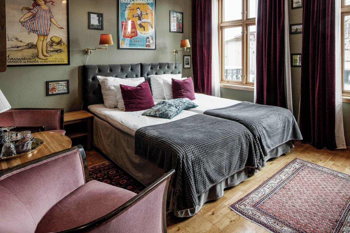 Ein ordentlich eingerichtetes Schlafzimmer mit einem großen Bett, zwei Nachttischen, einem Sessel und einem Fenster mit Vorhängen.