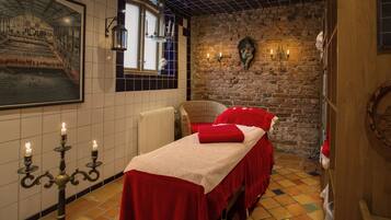 Una habitación con cama, una silla, un muro con un mural y un candelabro con velas.