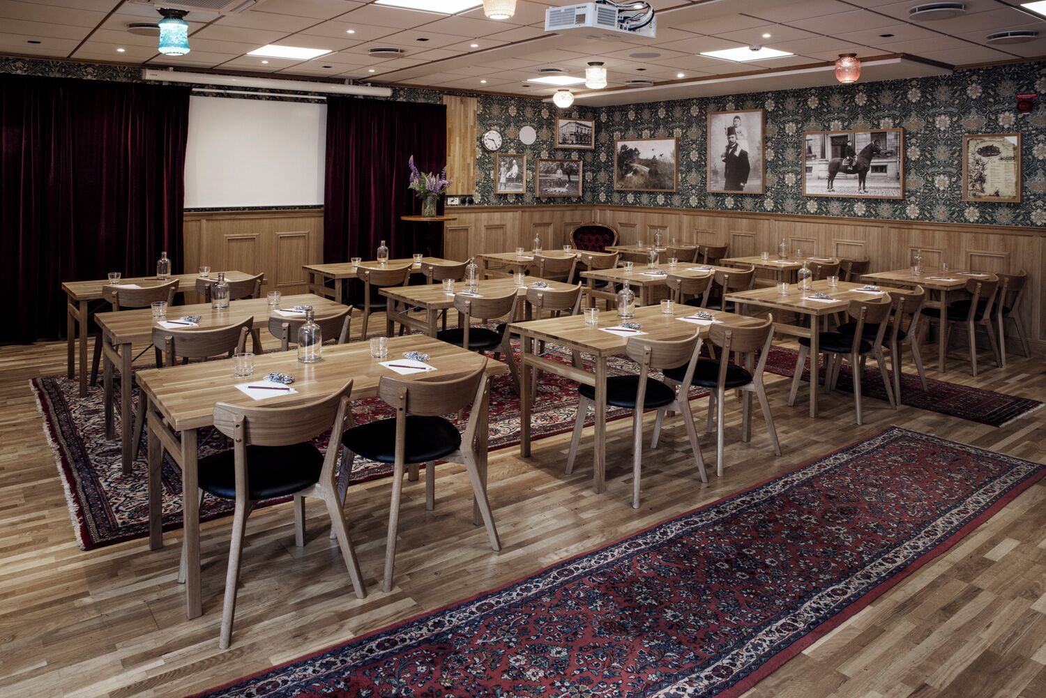 A conference room with wooden tables and chairs, a projector screen, and a stage with curtains.
