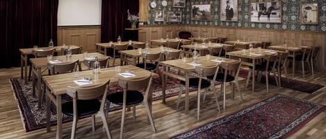 A conference room with wooden tables and chairs, a projector screen, and a stage with curtains.