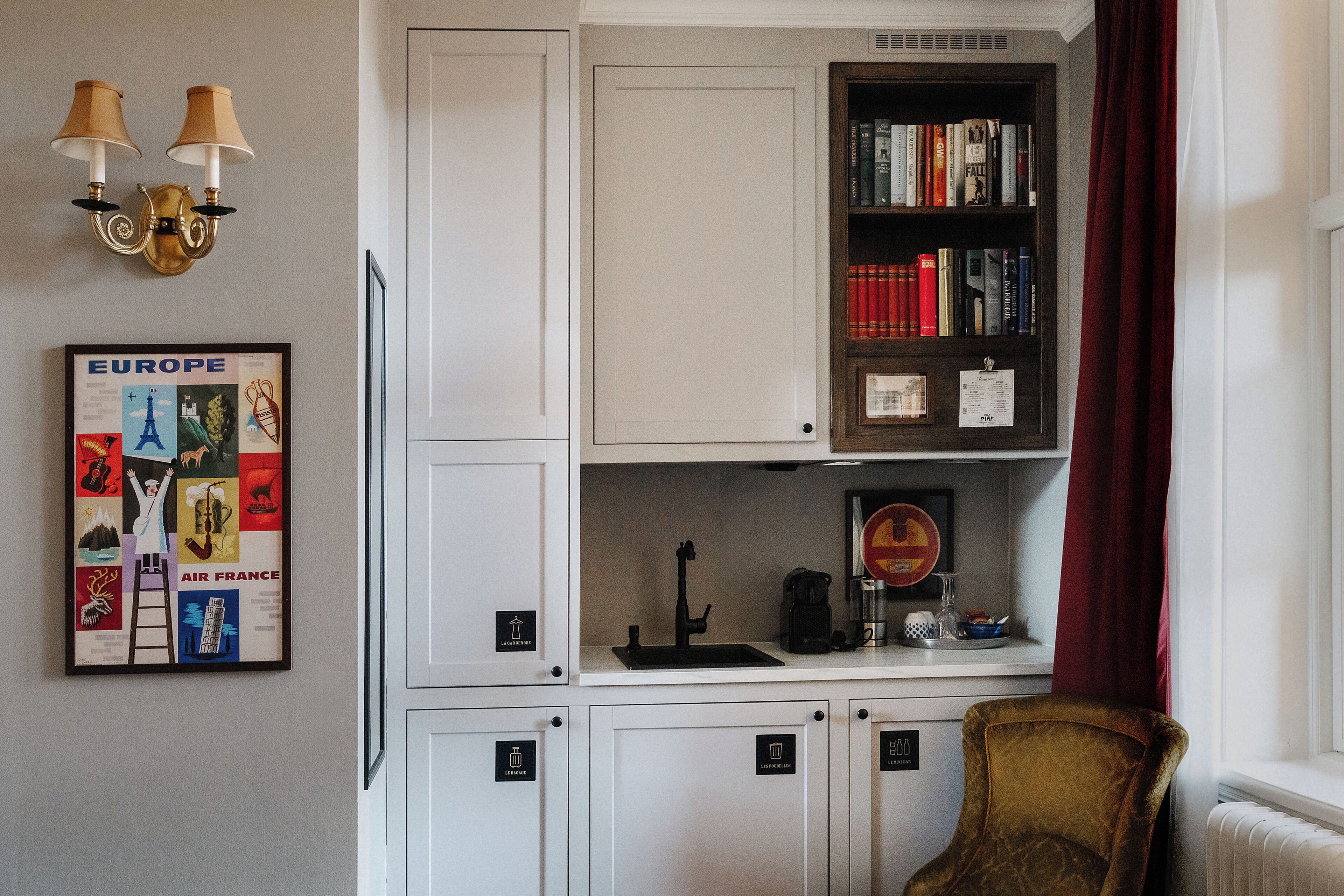 A room with a bookshelf, a framed map of Europe, a radiator, and a chair.