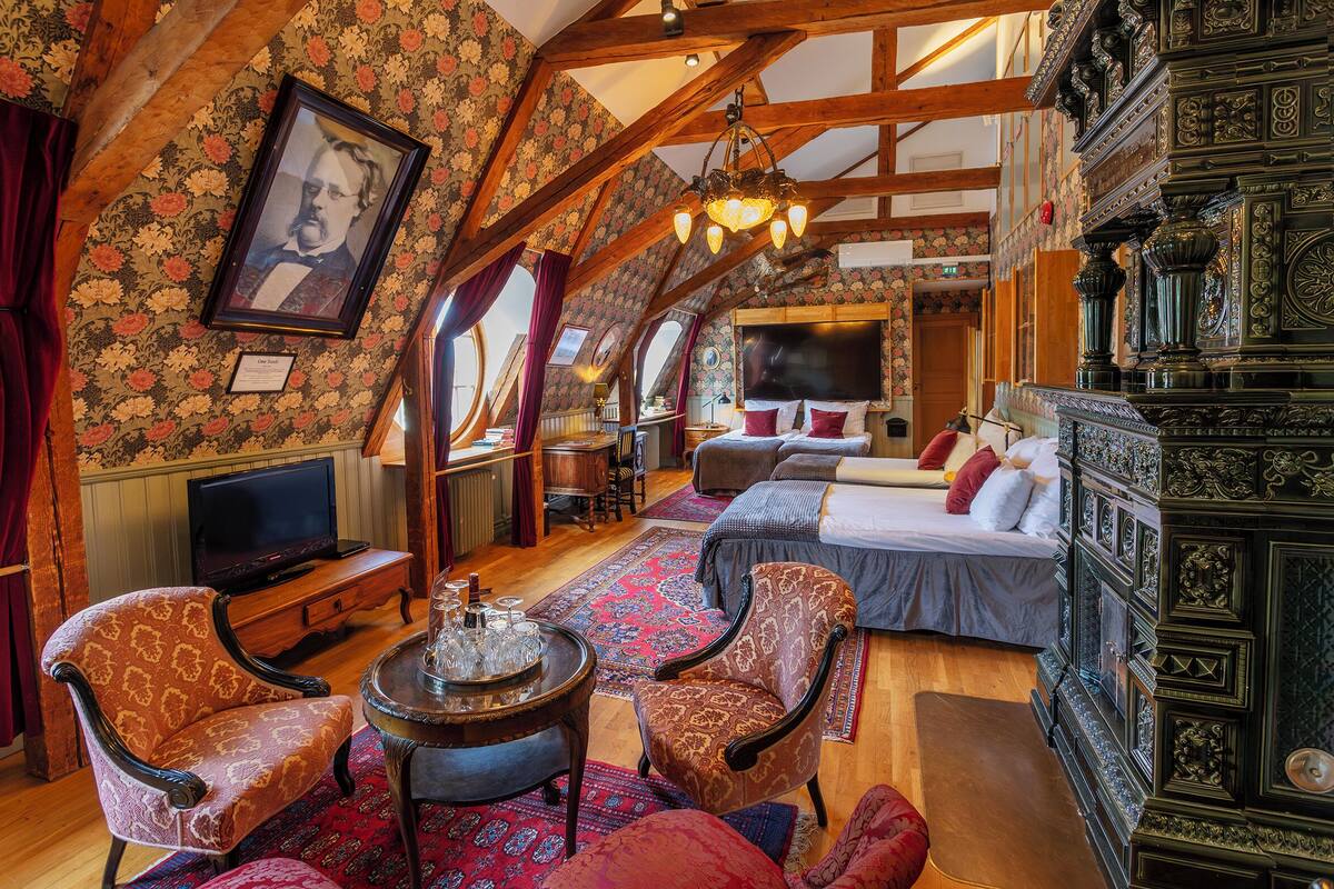 Ein Zimmer mit einem Bett, zwei Stühlen, einem Fernseher und einer Holzbalkendecke.