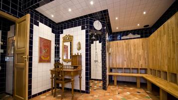 Un baño con suelo de baldosas, taquillas de madera, un espejo y un banco de madera.