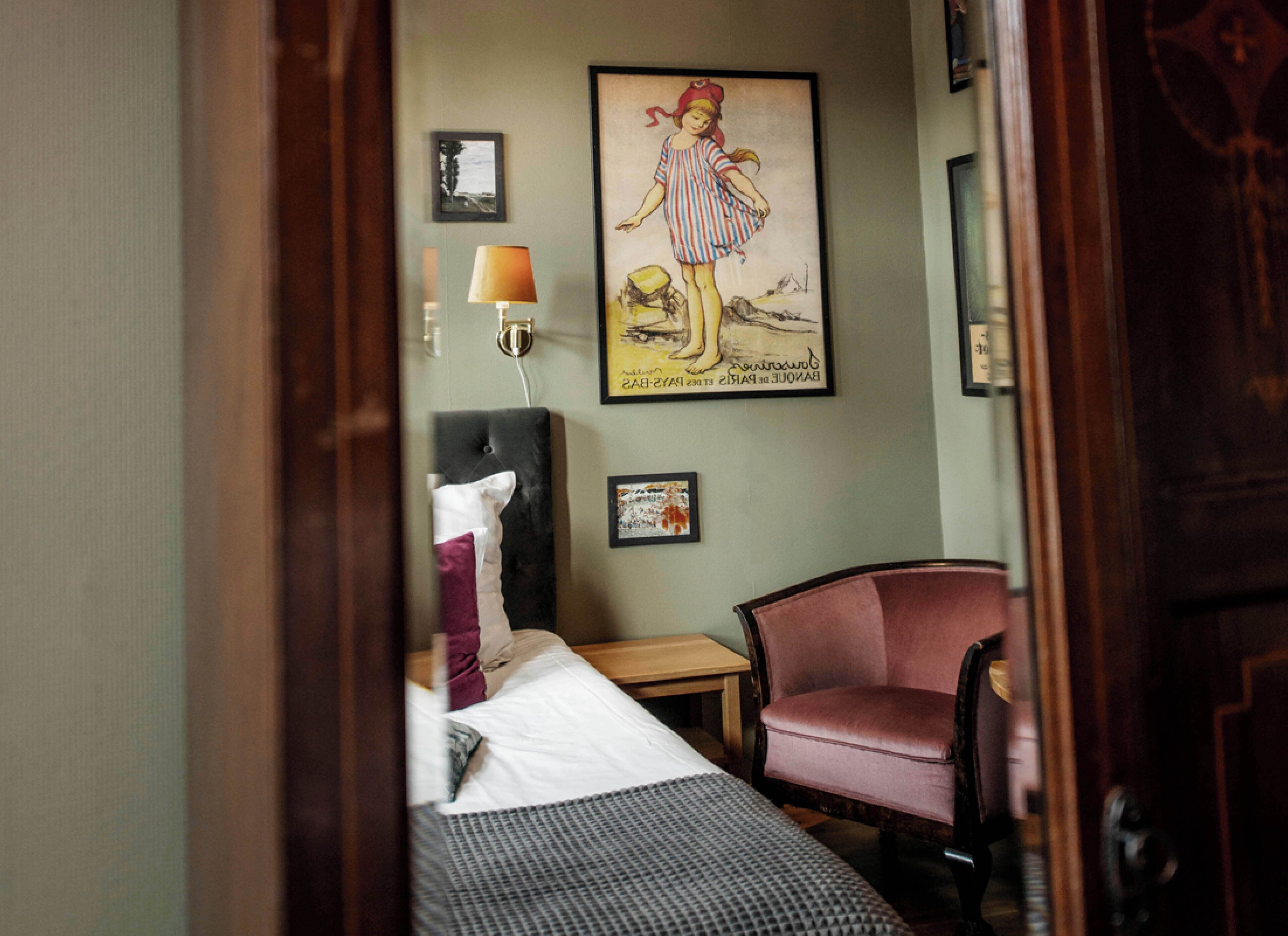 Una habitación de hotel con una cama, una silla, una lámpara y un cuadro en la pared.