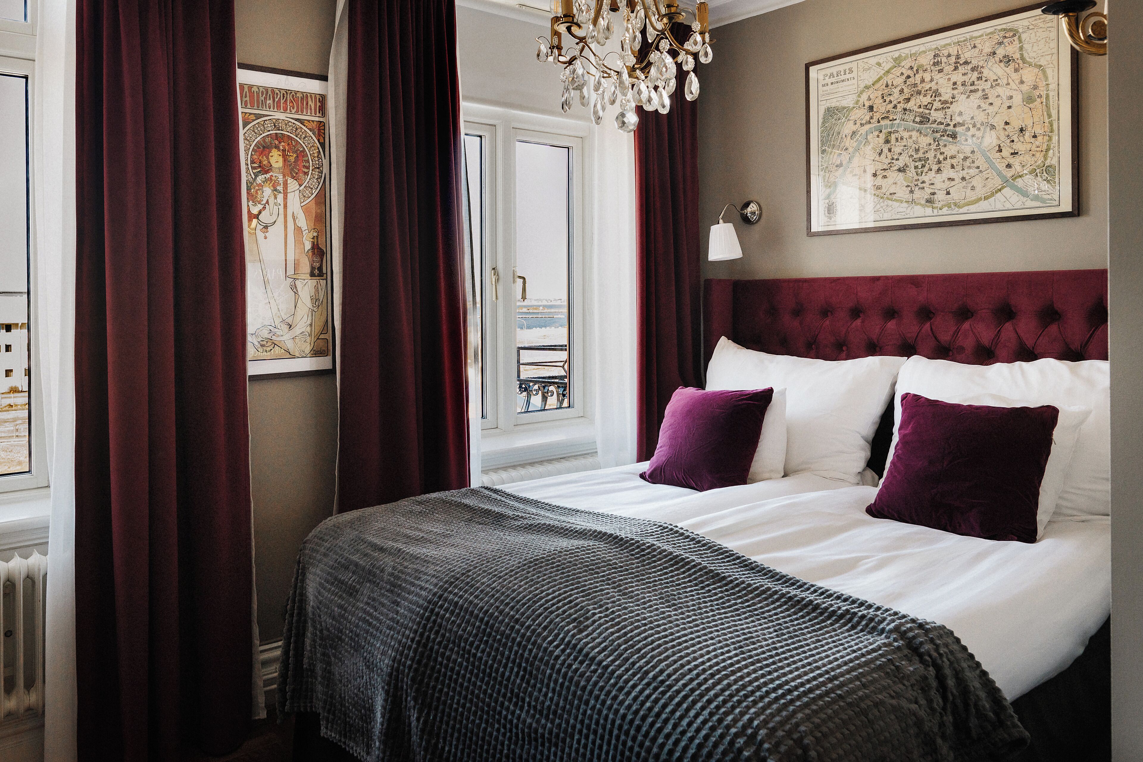 Une chambre à coucher avec un grand lit, un lustre, une carte accrochée au mur et une fenêtre avec des rideaux.