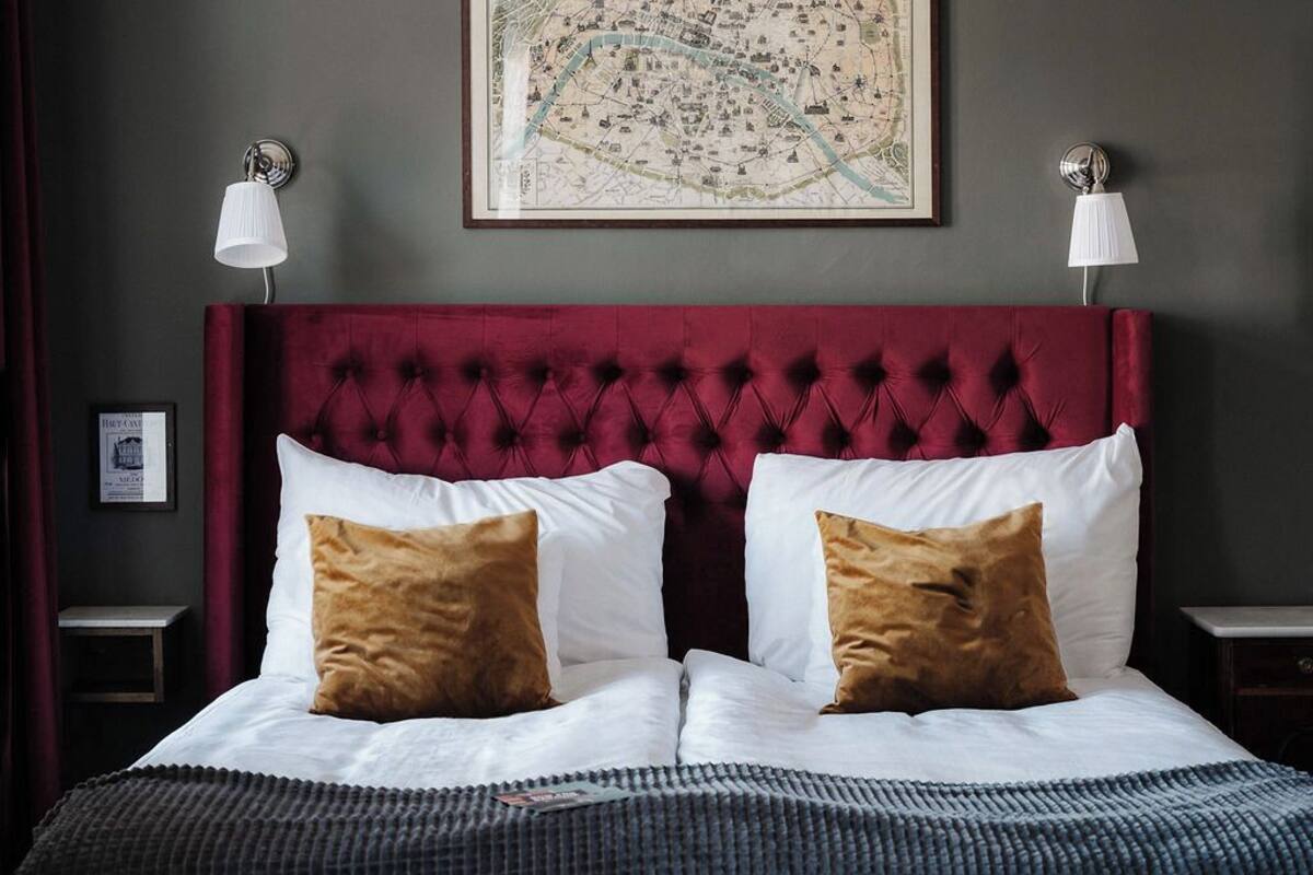 Ein Bett mit roter Kopfteil, weißen und braunen Kissen, einer gerahmten Karte an der Wand und zwei Nachttischlampen.