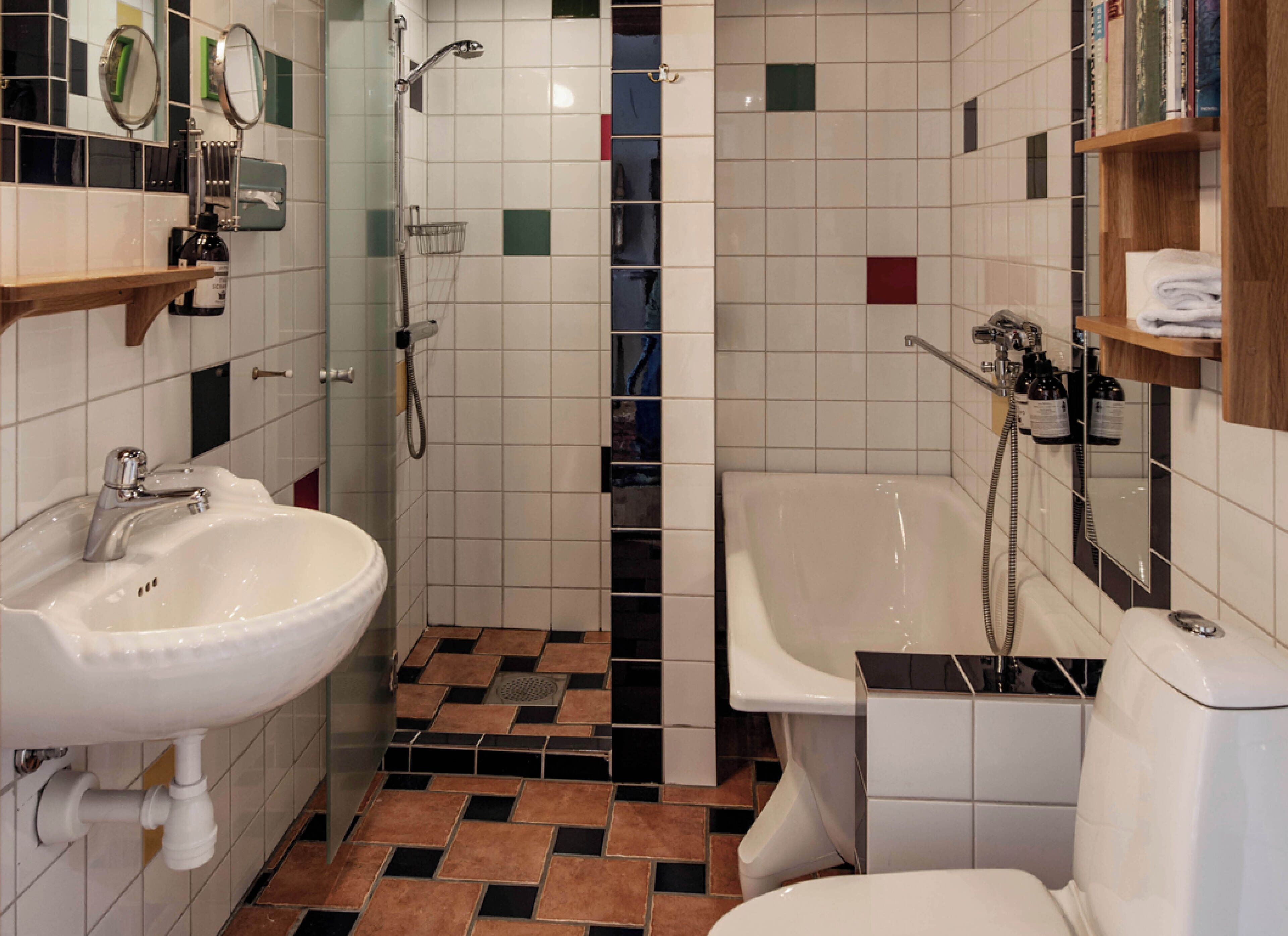 A bathroom with a sink, toilet, and bathtub. There are mirrors above the sink and bathtub, and a showerhead above the bathtub. The floor has a patterned tile design.