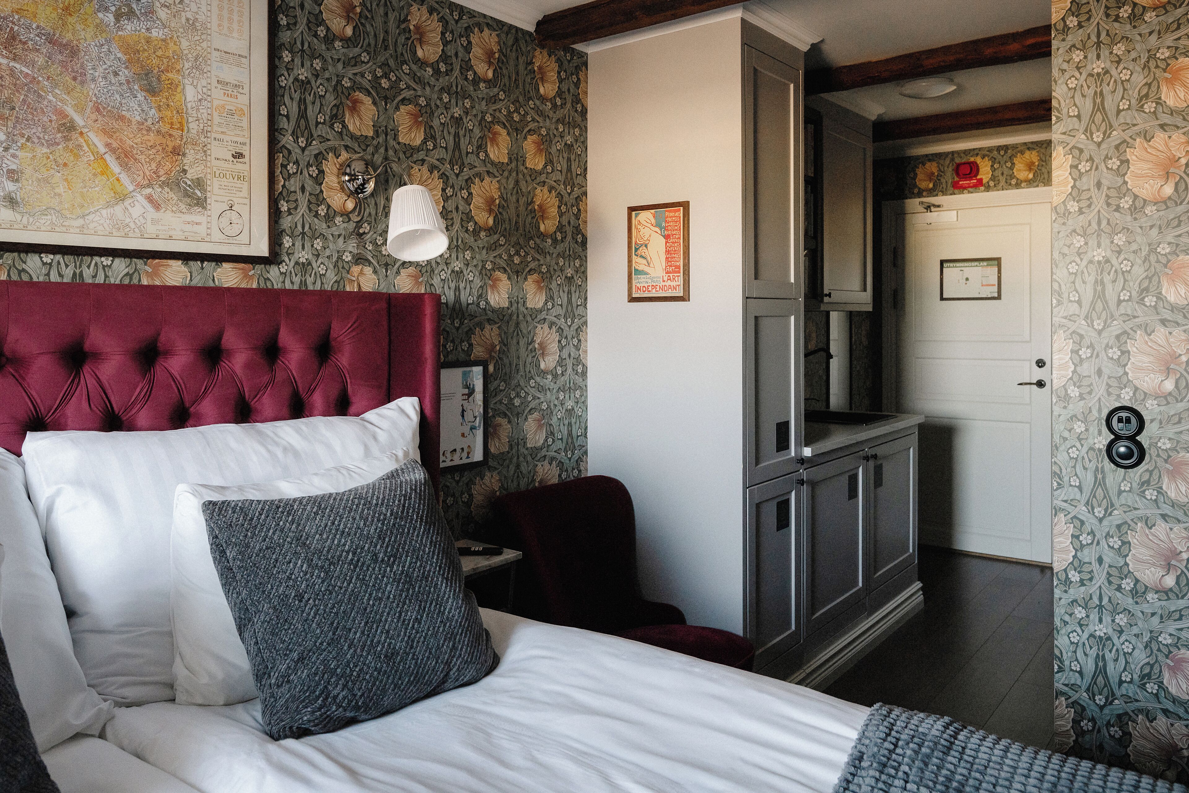 A bedroom with a tufted headboard, a bed with white and gray bedding, a red chair, a small table, and a map on the wall.