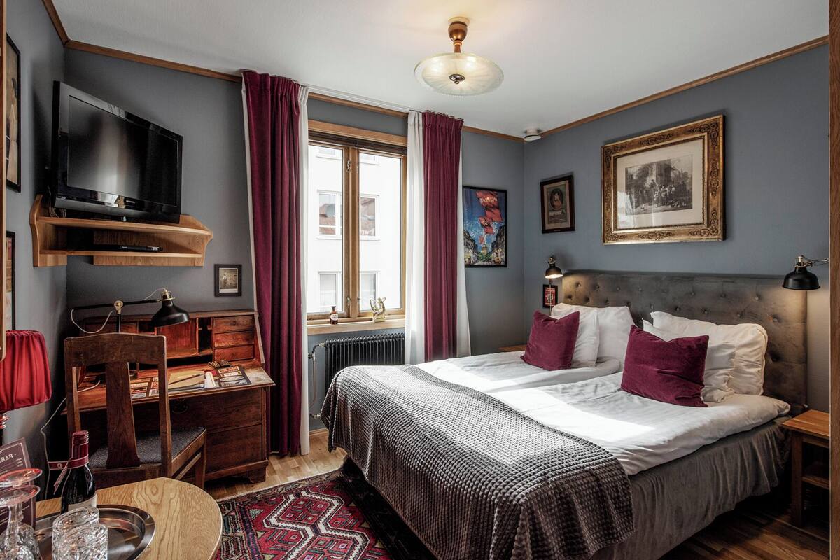 Ein Schlafzimmer mit einem Bett, einem Schreibtisch, einem Fernseher und einem Fenster mit Vorhängen.