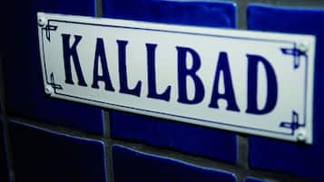 Un cartello stradale con la scritta "KALLBAD" fissato a una parete rivestita di piastrelle blu.