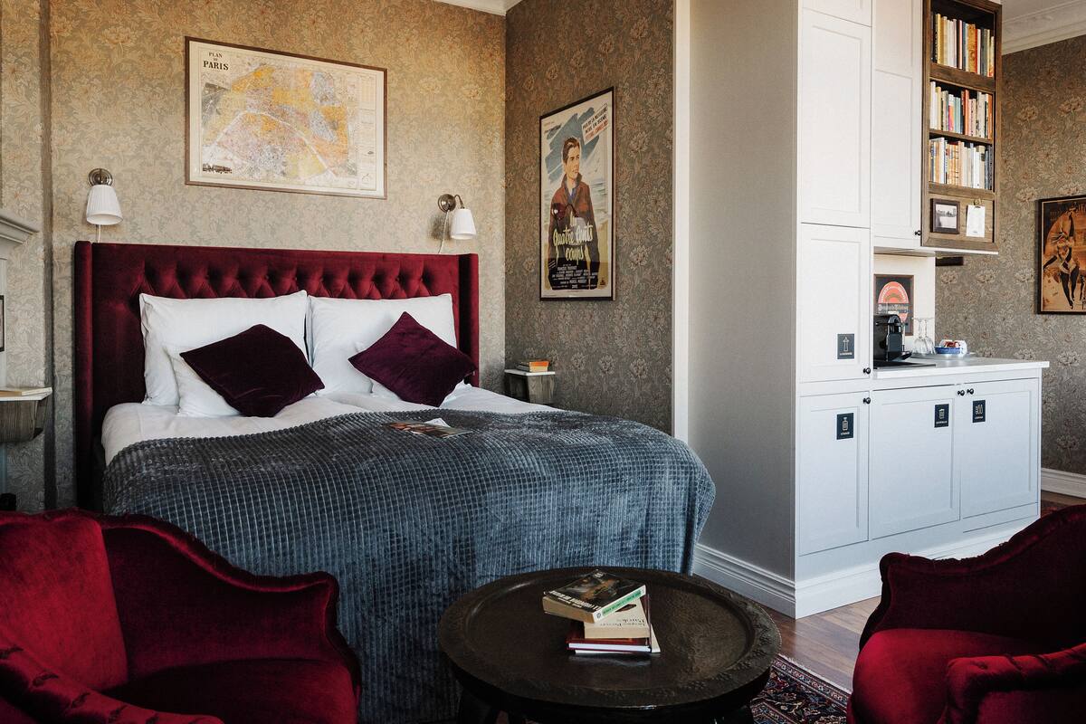 Ein Hotelzimmer mit einem großen Bett, einem kleinen Tisch, einem Bücherregal und einer Karte an der Wand.