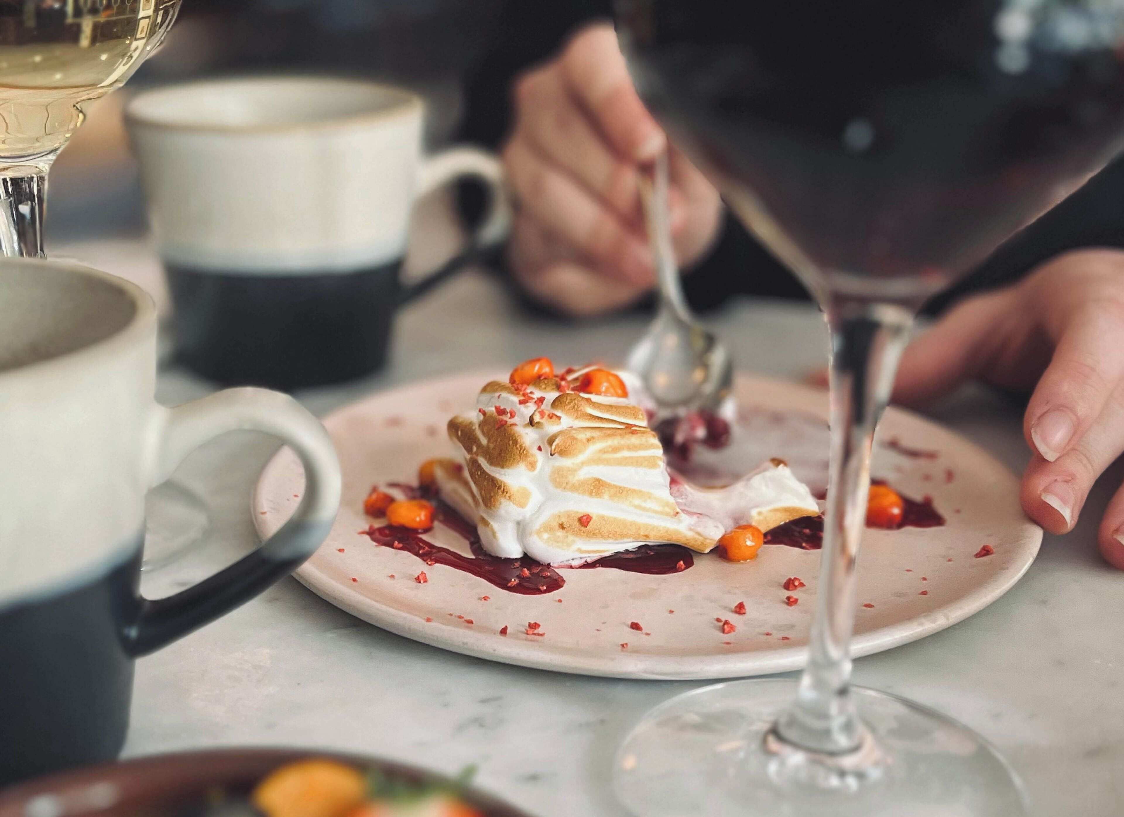 A dessert on a plate with a wine glass and a cup in the background.