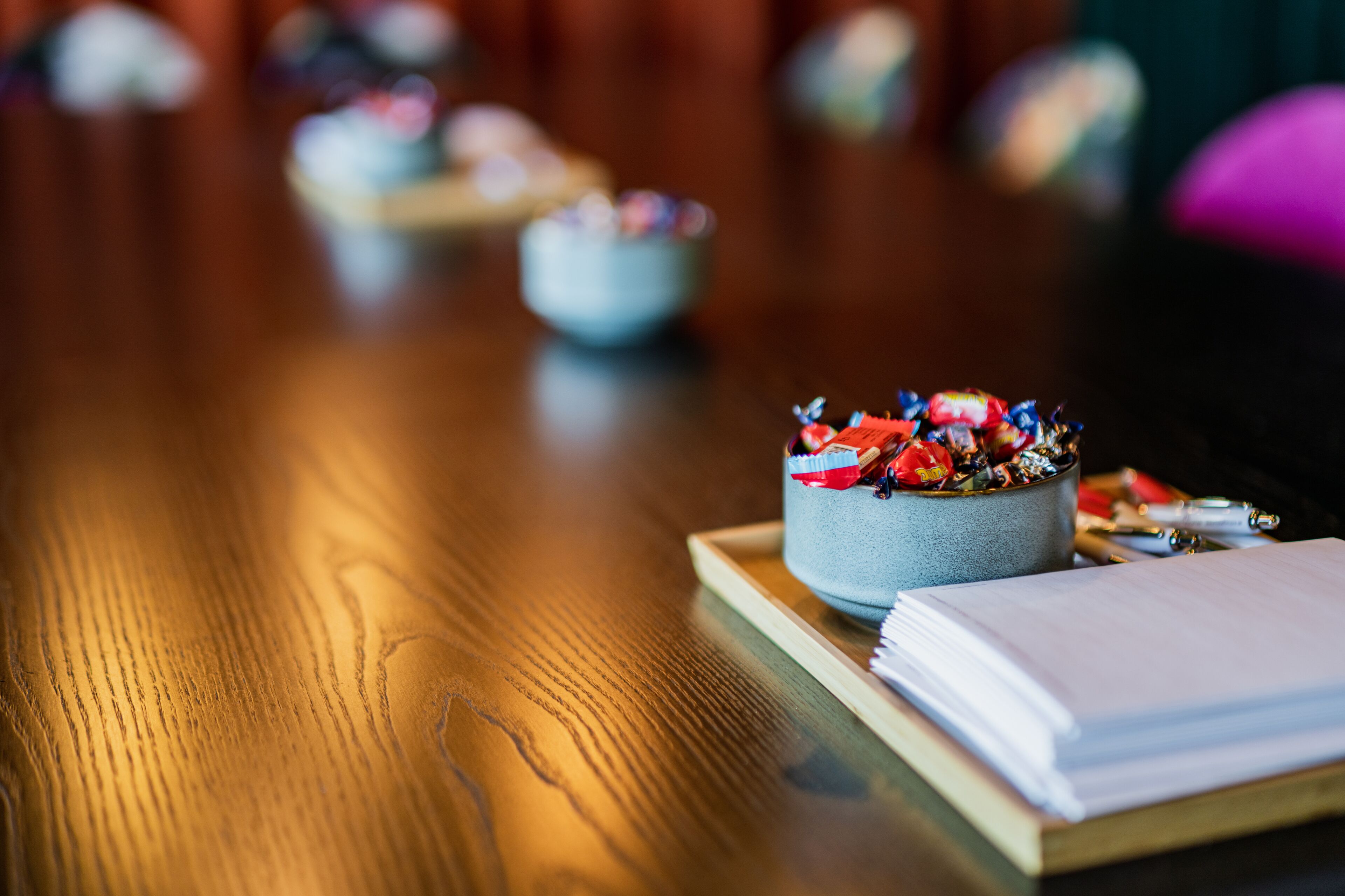 A wooden table with a bowl of colorful candies, a notebook, and pens.