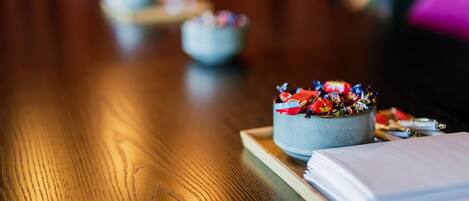 A wooden table with a bowl of colorful candies, a notebook, and pens.