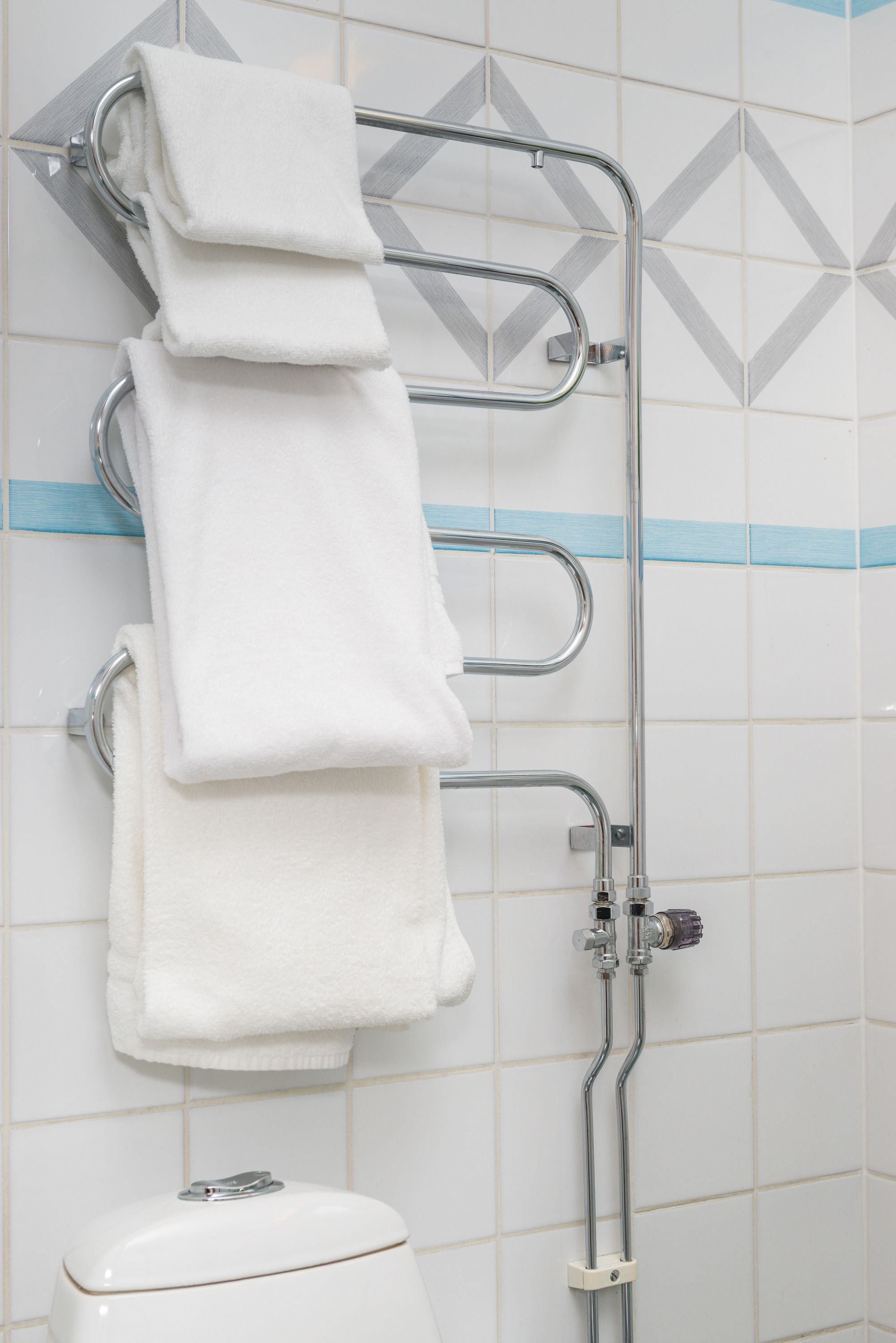 Casa de banho com parede revestida a azulejos brancos, um porta-toalhas com três toalhas e uma sanita.