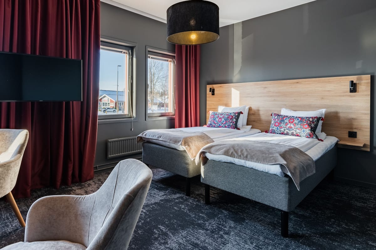 A modern hotel room with a large bed, two bedside tables, a flat-screen TV, and a window with curtains.