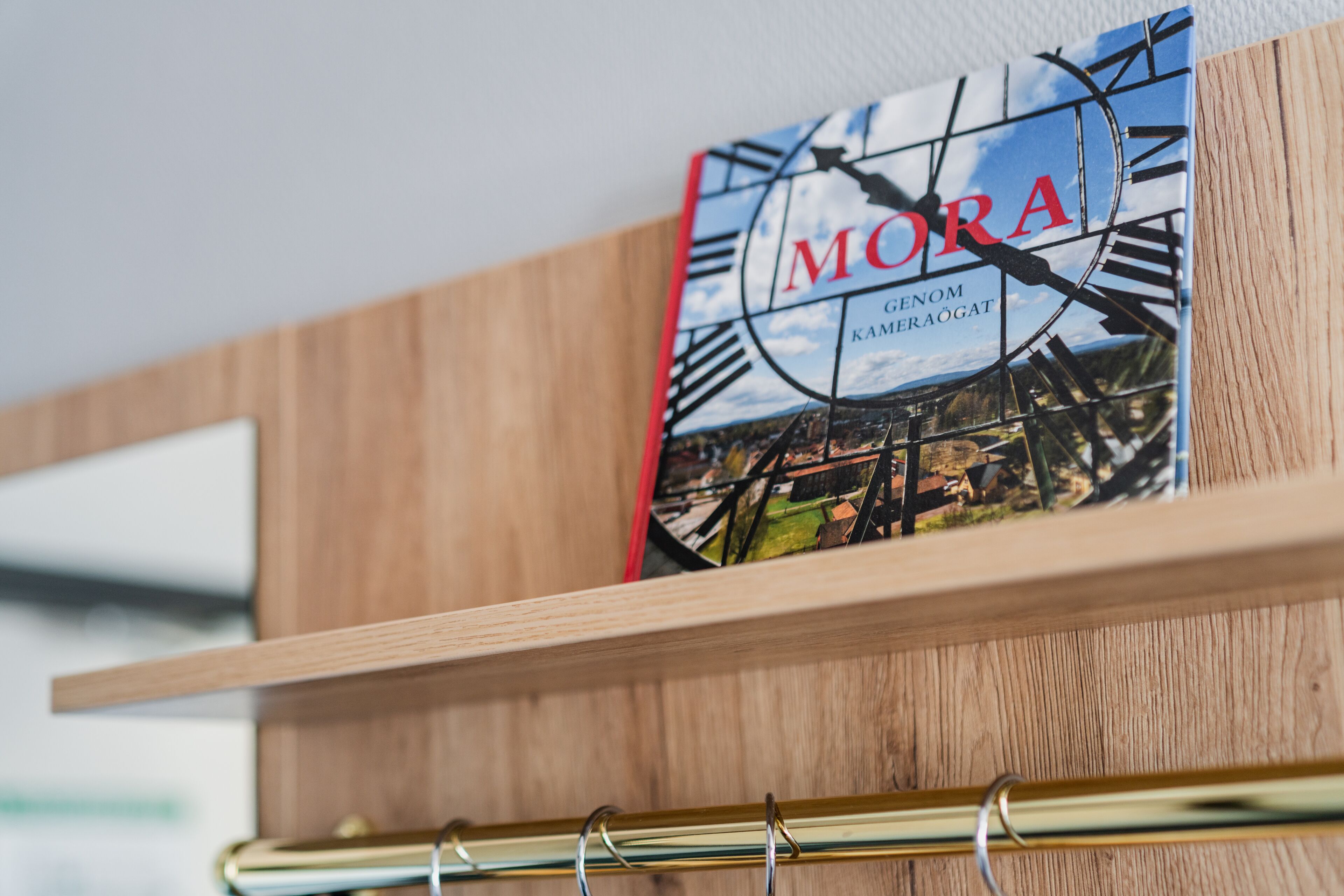 A wooden shelf with a book titled 'MORA' and a metal ring.