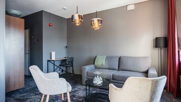 Un salon moderne avec un canapé gris, deux fauteuils, une table basse et des luminaires suspendus.