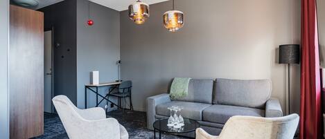 Una sala moderna con un sofá gris, dos sillones, una mesita de centro e iluminación colgante.