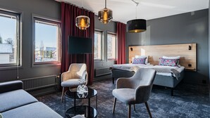 A modern hotel room with a large bed, two armchairs, a small table with glasses, and a TV. - Hotell Fridhemsgatan (Mora)