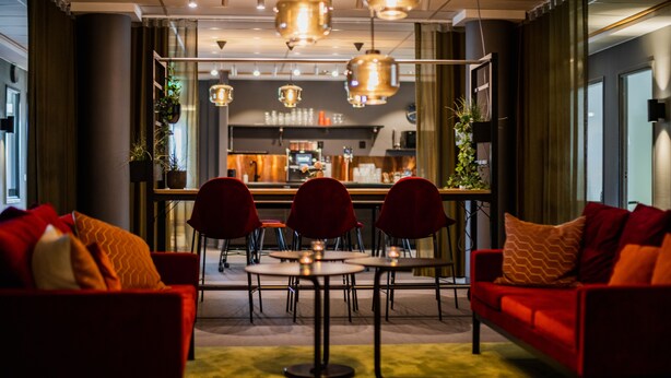 A modern hotel lobby with red sofas, round tables, and hanging pendant lights. - Hotell Fridhemsgatan (Mora)