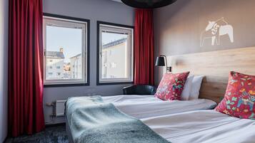 A hotel room with a bed, two windows, a radiator, a lamp, and a wall with a horse and rider mural.