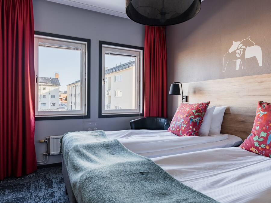 A hotel room with a bed, two windows, a radiator, a lamp, and a wall with a horse and rider mural.